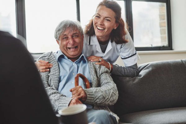Female carer and senior man laughing and looking at a woman sitting in front