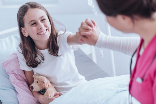 High angle of girl with plush toy smiling and giving a high five with nurse in the hospital