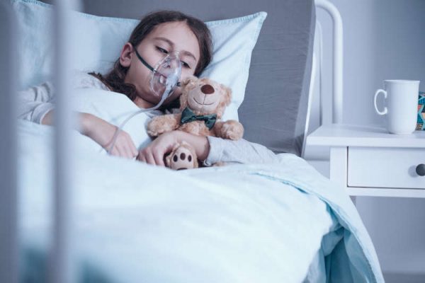 Kid with cystic fibrosis lying in hospital bed with oxygen mask and plush toy